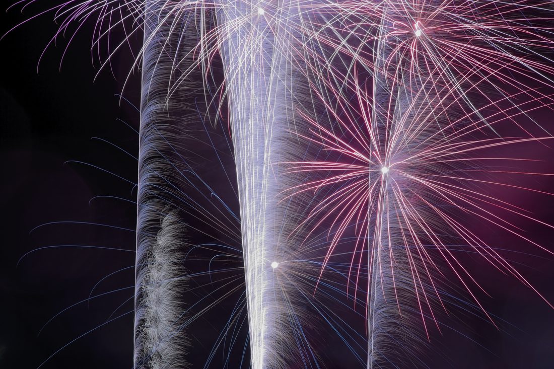 Pink and white firework trails streaking upward with red starburst accents