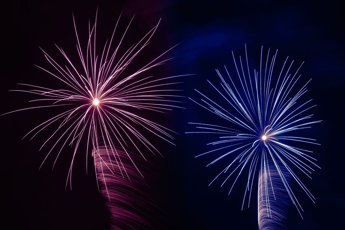 Twin fireworks bursting in synchronized pink and electric blue starbursts